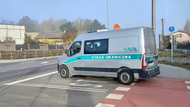 Pojazd Straży Granicznej stoi na skrzyżowaniu drogi z czerwoną ścieżką rowerową w słoneczny dzień.