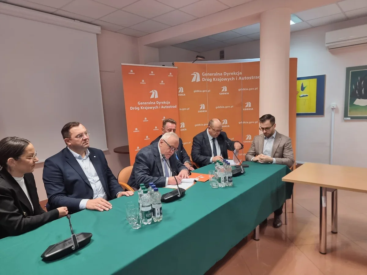 Grupa osób w strojach biznesowych siedzi przy stole podczas konferencji prasowej lub podpisania dokumentu w siedzibie Generalnej Dyrekcji Dróg Krajowych i Autos